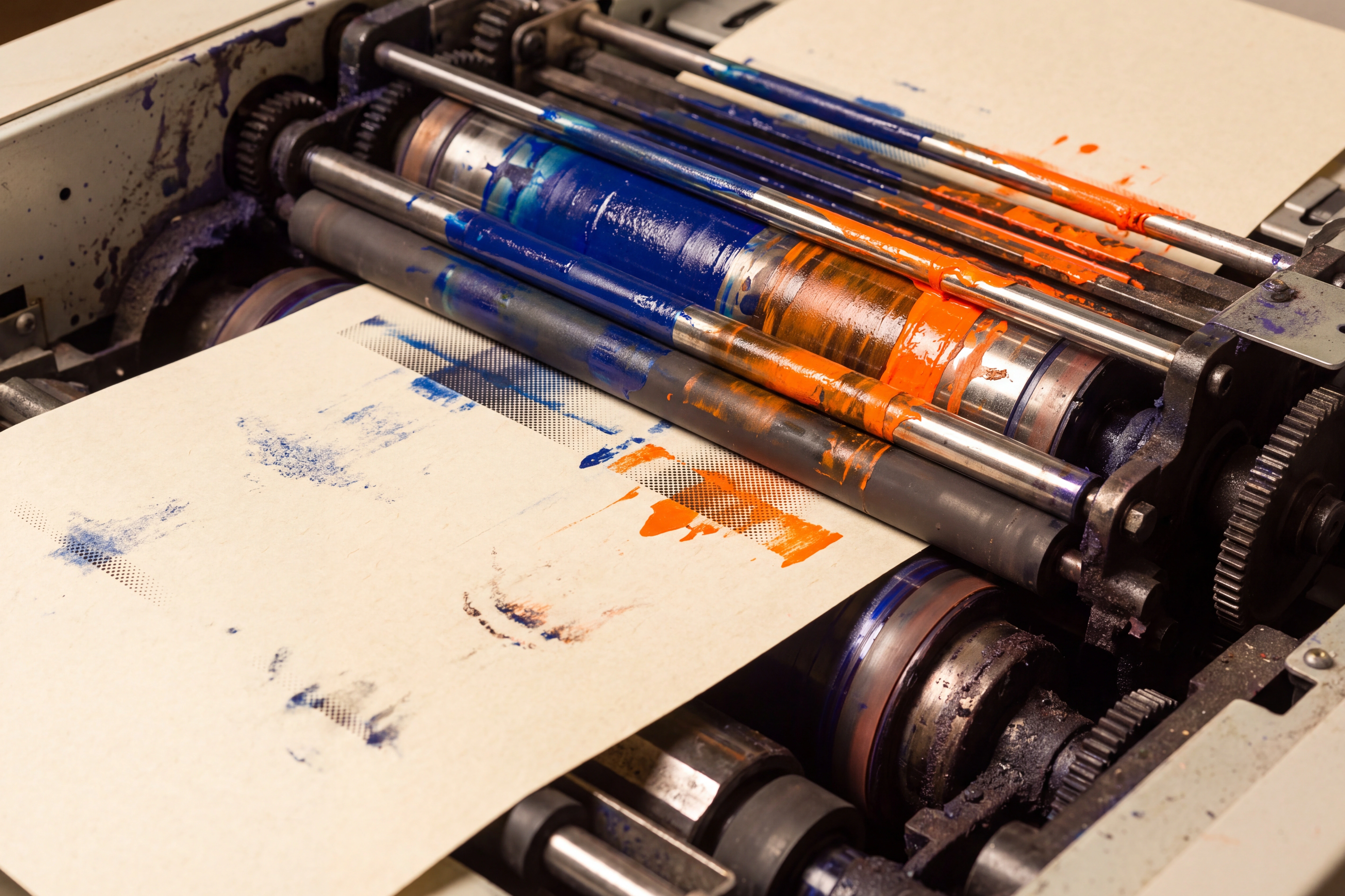 Risograph worktable with wet cobalt and orange ink, halftones, and misregistered sheets.