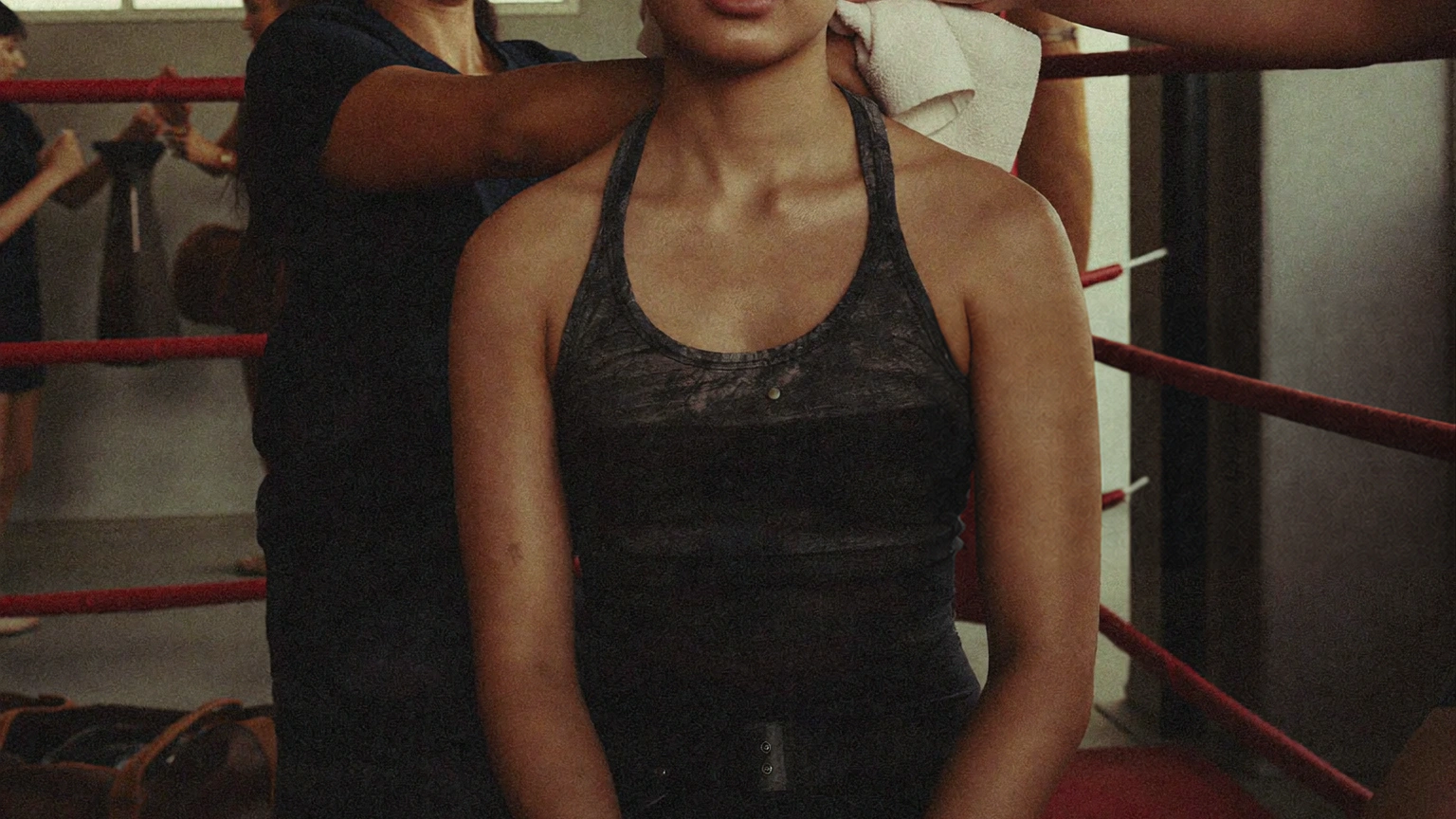 A boxer sits in the ring between efforts while the gym remains active around them.