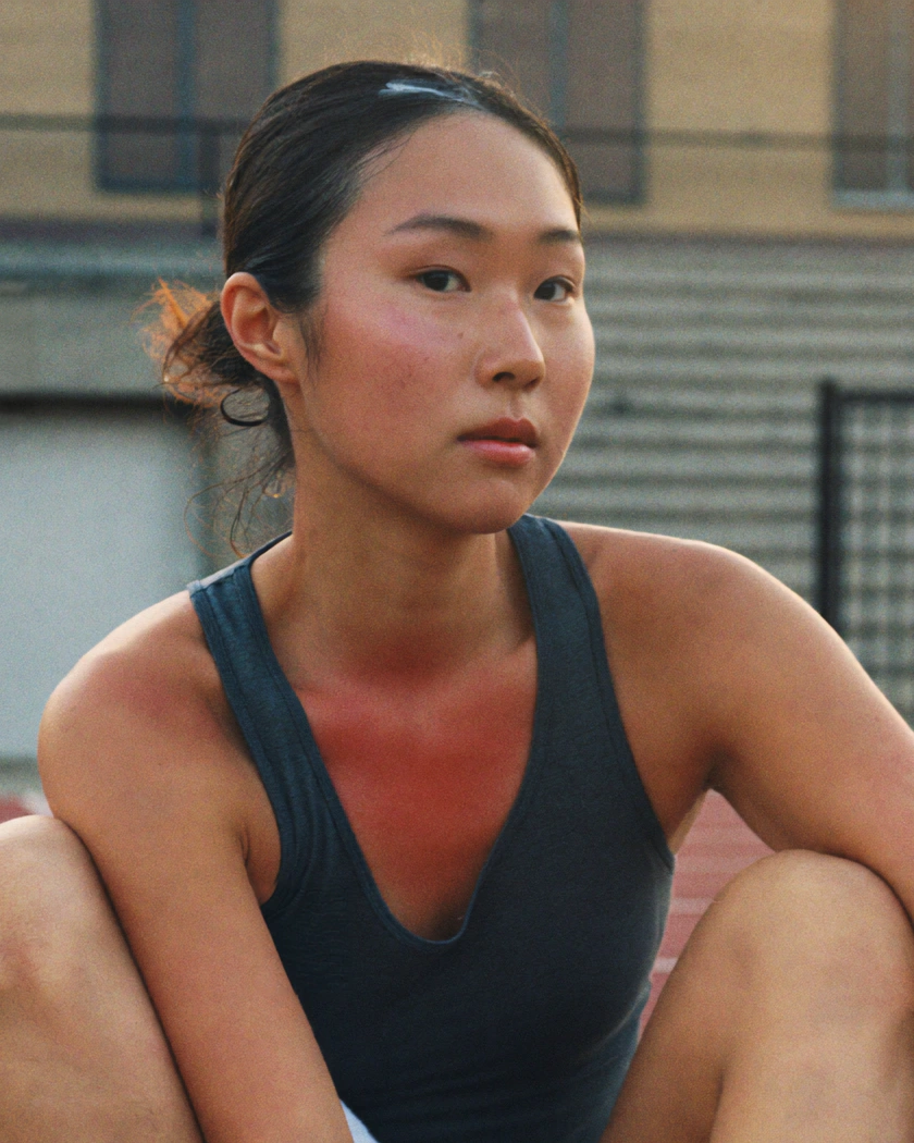 A perspiring athlete in a dark training top sits at rest beside a pale wall and steps.