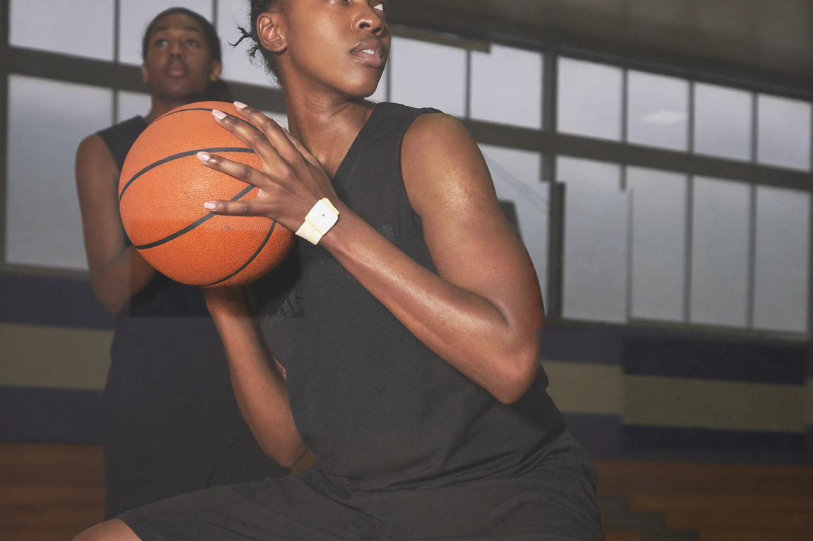 A basketball player holds the ball at chest height and turns toward the side of an indoor court.
