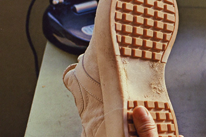 A hand holds the pale outsole of a tan shoe, showing raised square tread and visible wear.