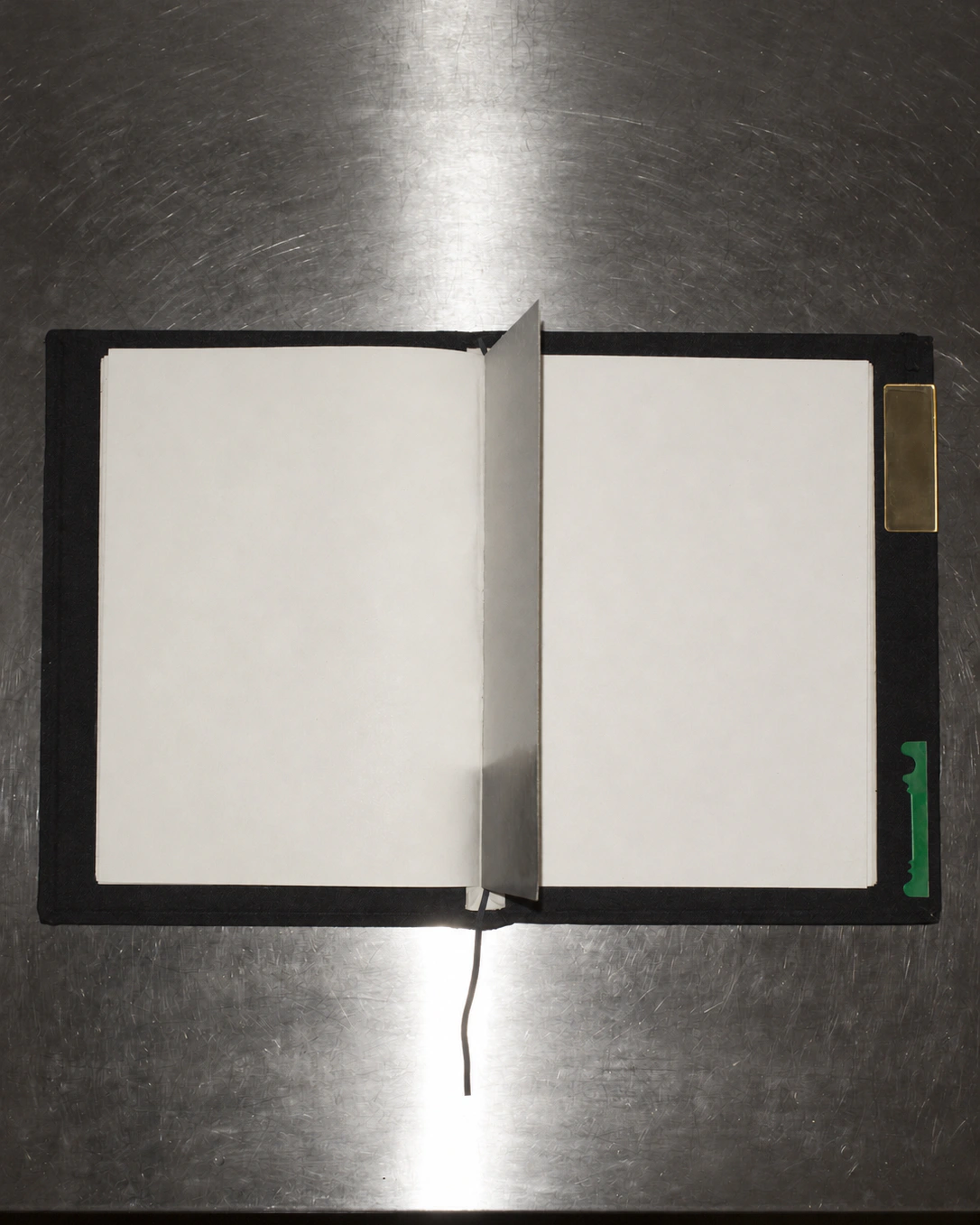 An open cream notebook with a black cover sits beside a steel divider on a reflective platform.
