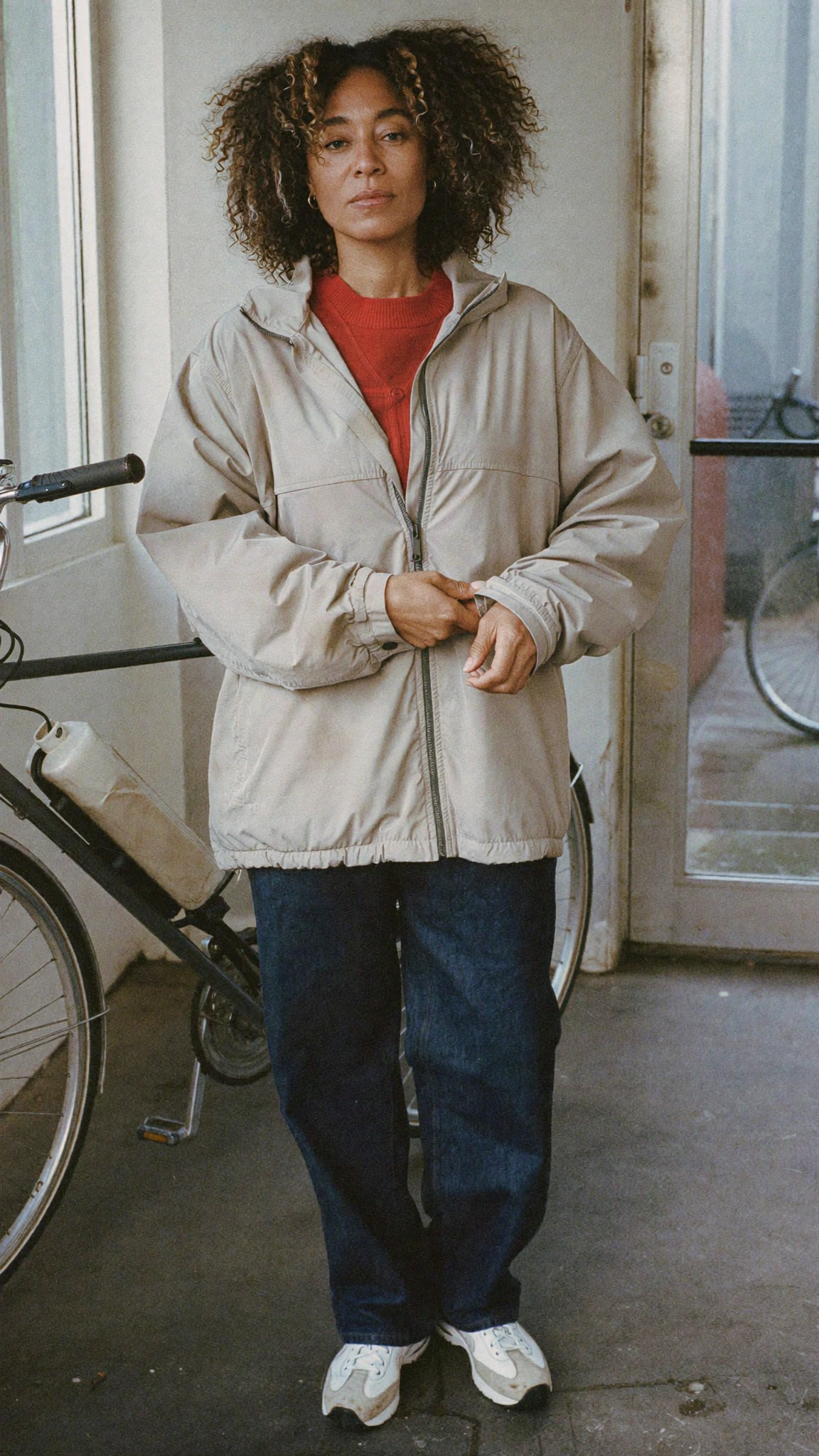 A woman standing beside a bicycle in a doorway, wearing everyday layers.