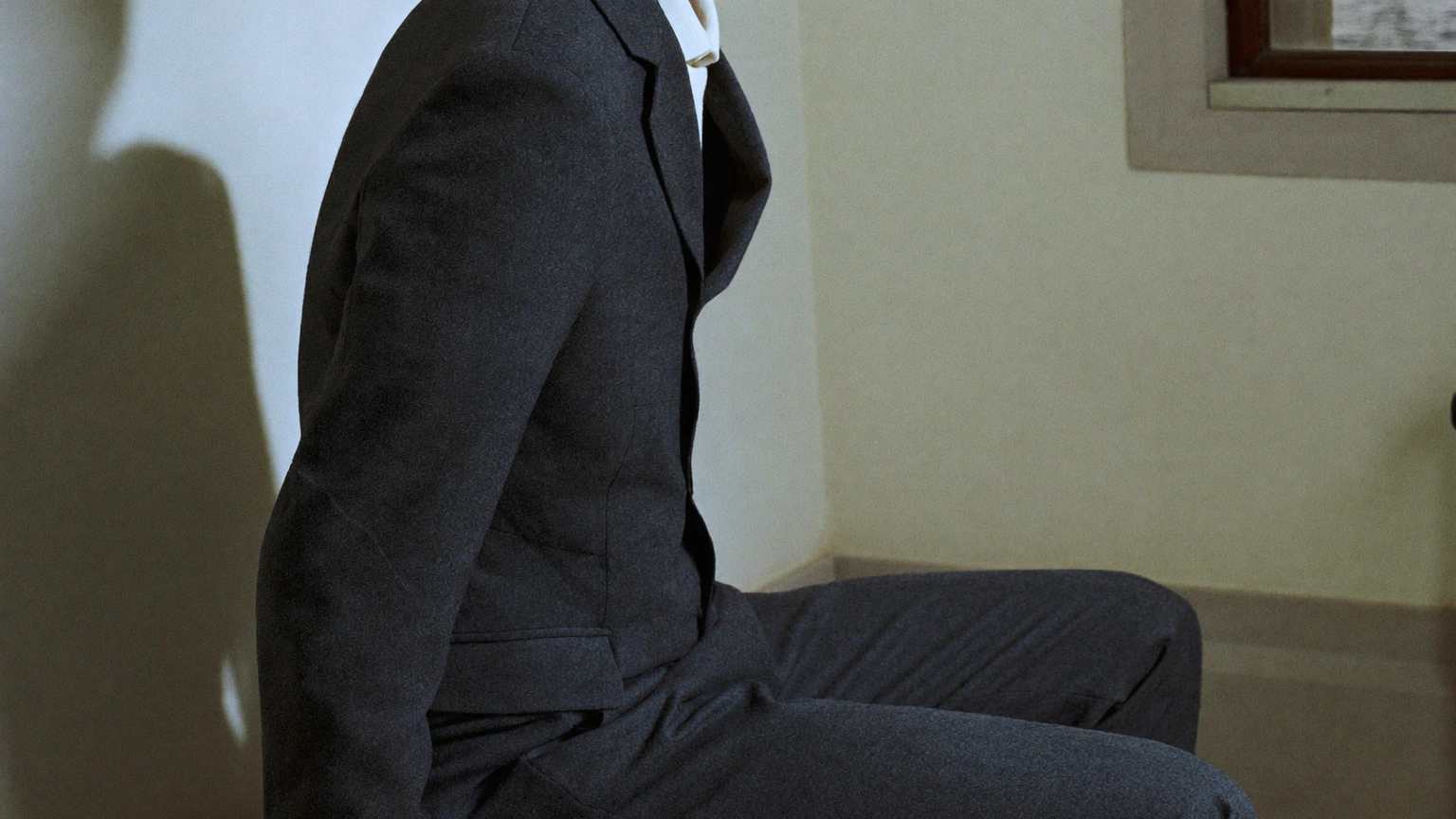 Close crop of a seated person's charcoal jacket, pocket, sleeve and tailored trousers.